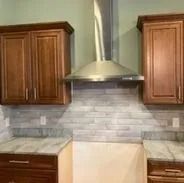Kitchen with cabinets, vent hood, and stone backsplash.