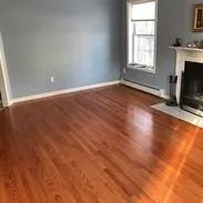 Empty room with hardwood floor, light blue walls, a window, and a fireplace.