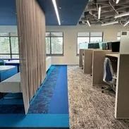 Office space with blue and gray carpets, cubicles, and a curtain.
