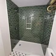 Green tiled shower with a built-in shelf and white base.