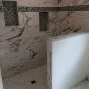Marble-tiled shower with built-in shelves and a decorative accent, showcasing a bright and modern design.