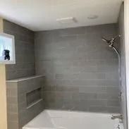 Bathroom with gray tiled walls, bathtub, showerhead, and recessed shelf.