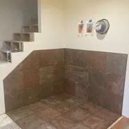A corner in a room with brown tiles on the floor and wall. Stairs are on the left.