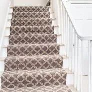 Carpeted stairs with patterned beige and brown design and white railing.