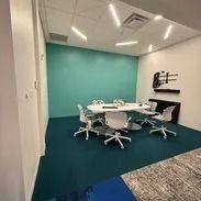An empty teal meeting room with a round table, chairs, and turquoise wall.