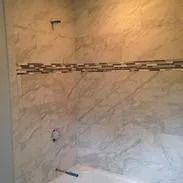 Bathroom wall with large marble-like tiles, a horizontal mosaic tile stripe, and a tub faucet.