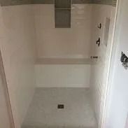 A white tiled accessible shower with built-in bench and grab bars.