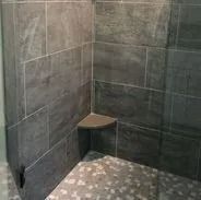 Gray tiled shower with a built-in corner seat; the shower floor has small, speckled tiles.