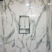 Shower with marble-look tiles and a recessed shelf. The tiles are white with gray veining.