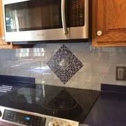 Kitchen with a microwave above a stovetop, blue countertop and backsplash with a mosaic accent.