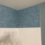 Blue mosaic tile border above white wall in a bathroom corner.
