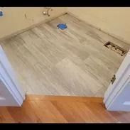 Tiled bathroom floor with light gray wood-look tiles, viewed from doorway.