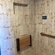 Wood-paneled shower with a foldable wooden seat, grab bar, and a small screen.