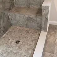 Bathroom shower with gray tile walls, built-in bench, and drain in the floor.