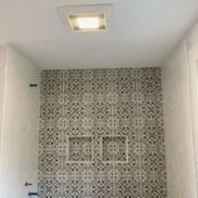 Bathroom shower with patterned tile wall, recessed shelves, and ceiling light.