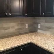Dark cabinets, granite countertop, and wood-look backsplash in a kitchen.
