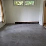 Empty room with gray floor, white walls, small window, and dark baseboard heater.