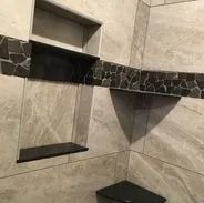 Tiled shower with built-in shelves and decorative dark rock border.