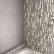 Bathroom with a gray tiled wall and patterned tile accent near the shower head and faucet.