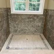 Shower with gray marble-like tiled walls, a window, and a beige-tiled floor with a decorative border.