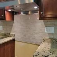 Kitchen backsplash of neutral-toned, horizontal tile with a stainless steel range hood; granite countertops.