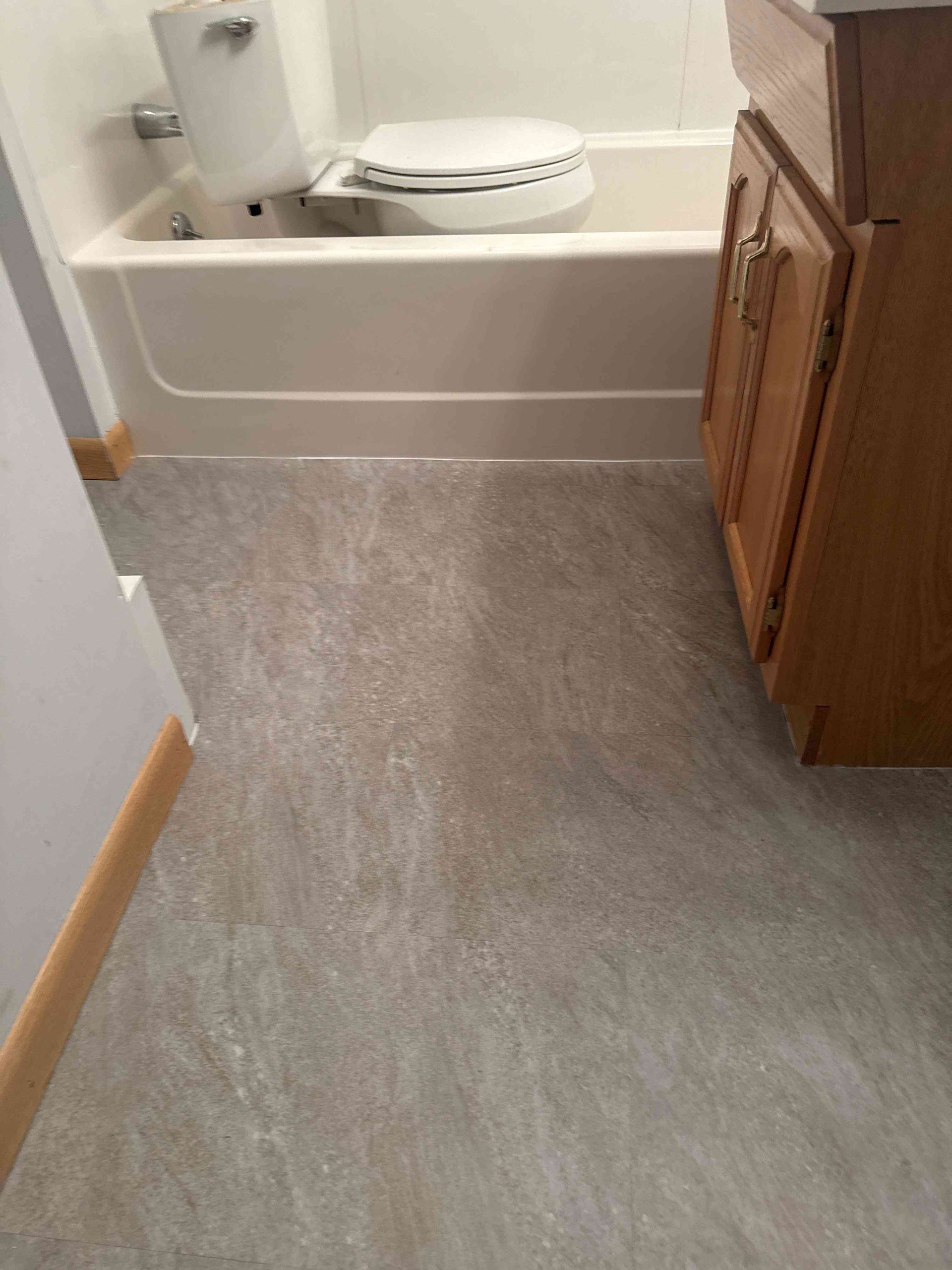 Bathroom with a toilet, bathtub, wooden vanity, and gray flooring.