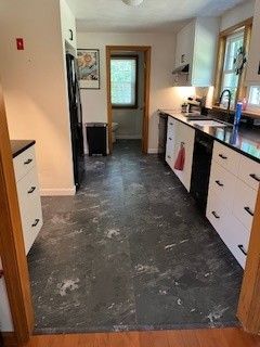 Kitchen with dark flooring, white cabinets, black appliances, and a door leading to a hallway.