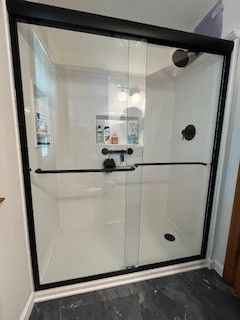 Black-framed shower enclosure with glass doors and a white interior. Black shower fixtures and a grab bar are visible.