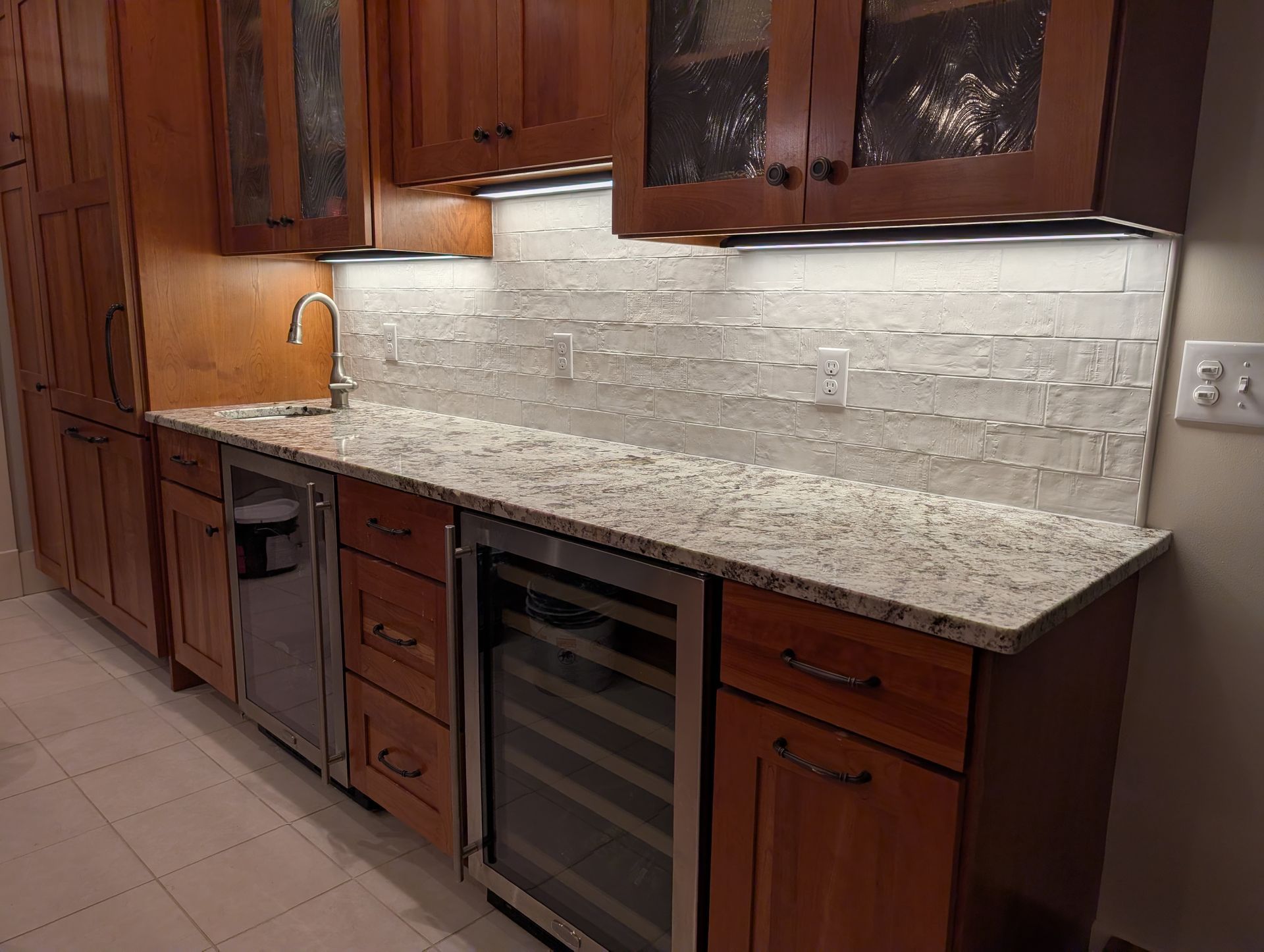 Kitchenette with wood cabinets, granite countertop, wine cooler, and tile backsplash.