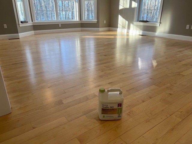 A bright hardwood floor with a can of floor finish in the center. Large windows and gray walls are in the background.