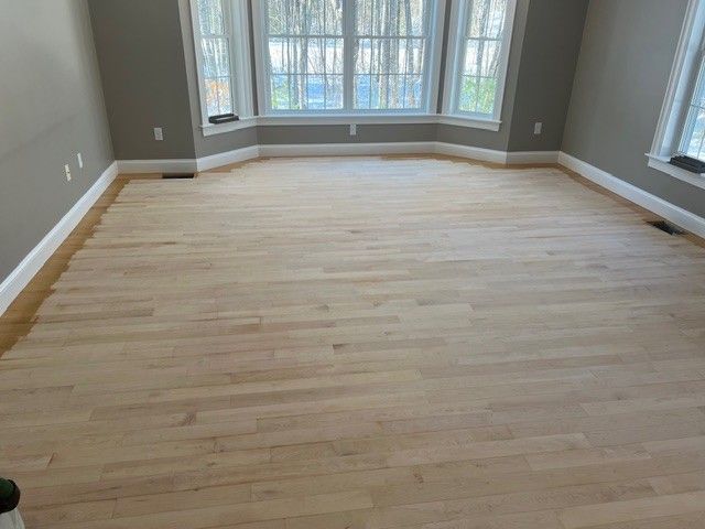 Light wood floor in a room with gray walls, white trim, and a bay window with a view.