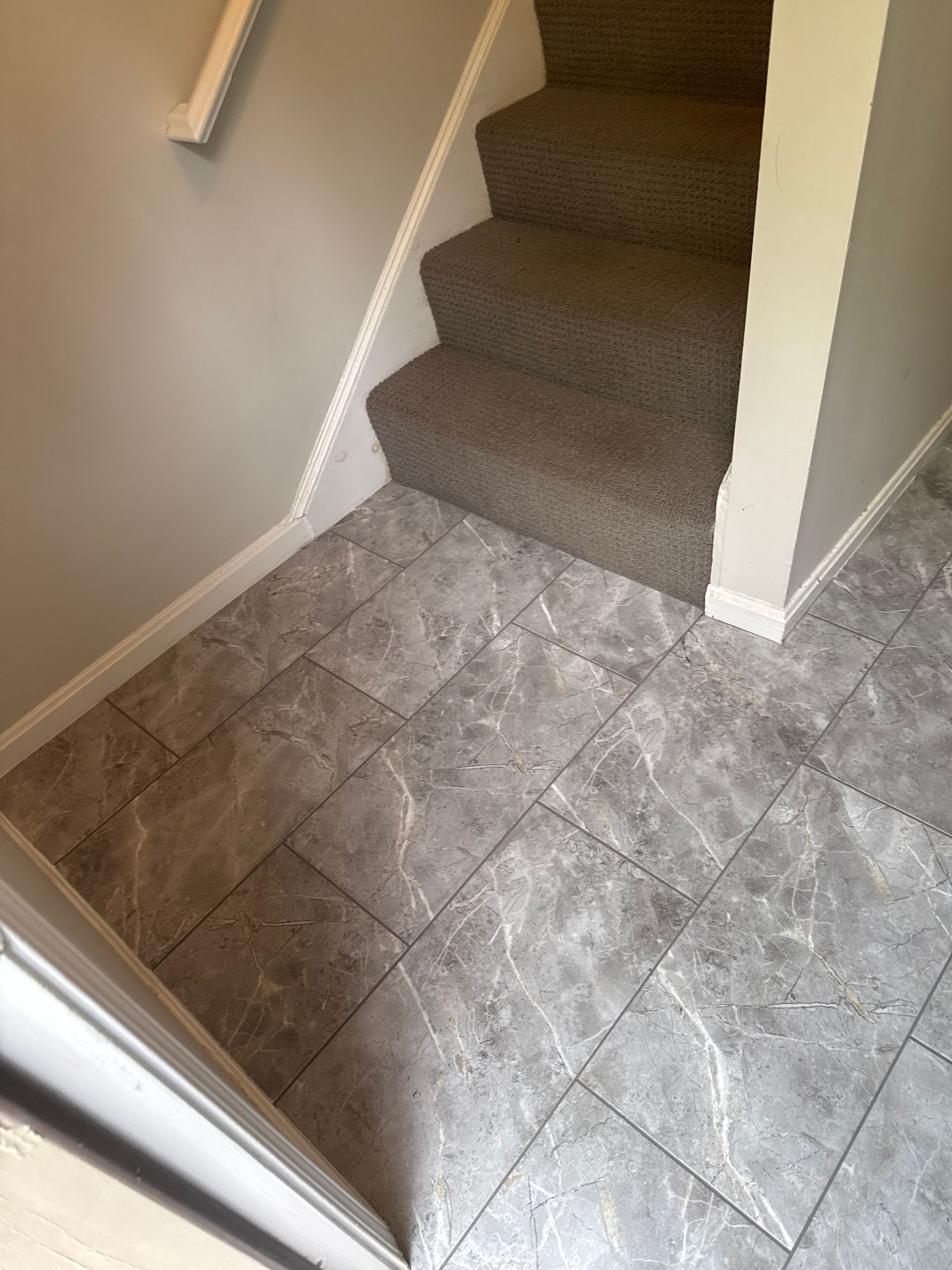 Gray tiled floor next to carpeted staircase. White trim and beige walls.