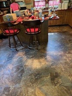Kitchen with worn, mottled flooring and bar stools. Person in pink shirt in background.