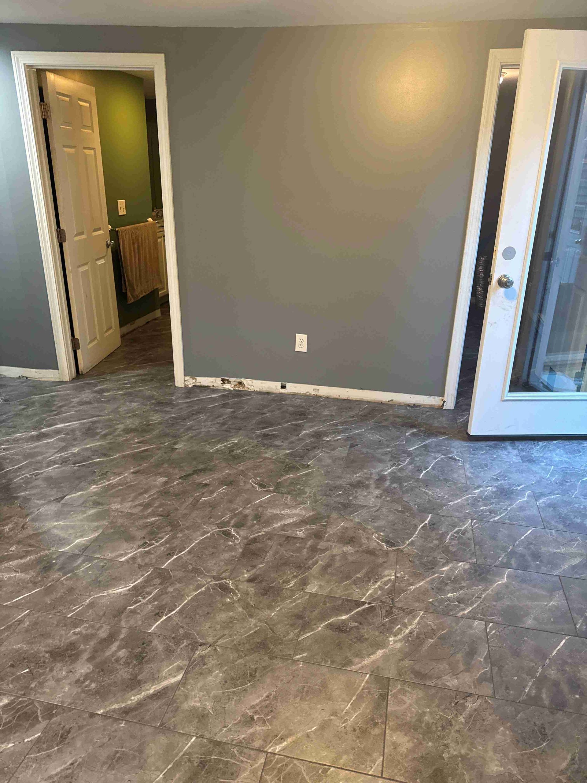 Room with gray walls, tiled floor, and doors leading to another room and outside.