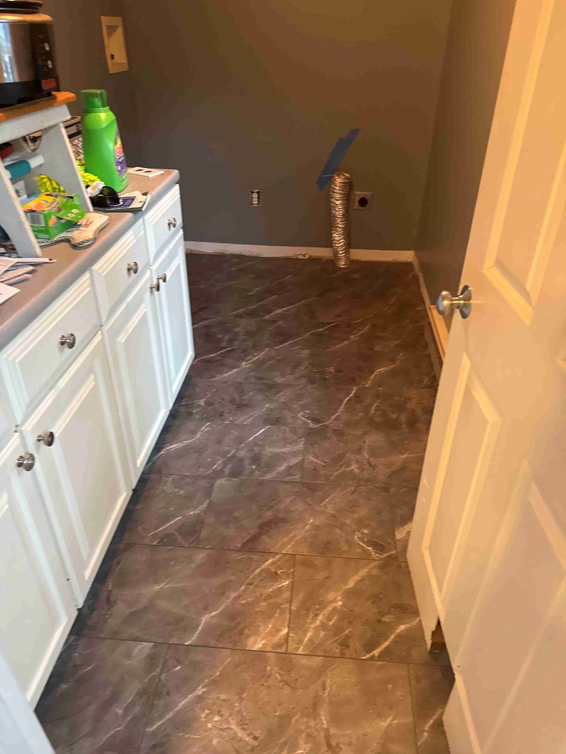 Laundry room: white cabinets, dark marbled floor, gray walls, open doorway, washer vent.