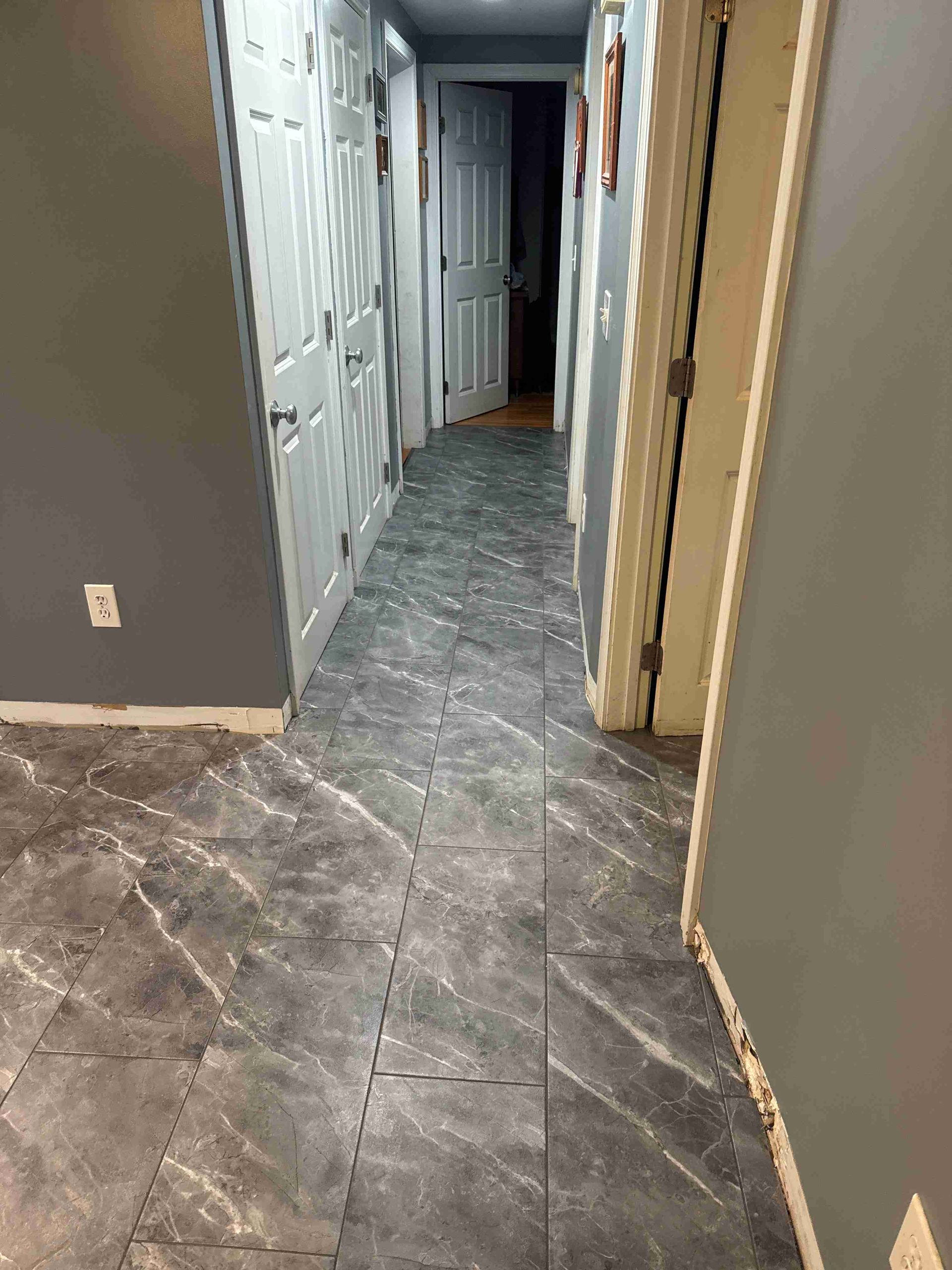 Hallway with gray walls and dark gray patterned flooring. Several white doors line the sides.