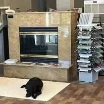 Black dog sitting in front of a fireplace with granite surround and display of tile samples.