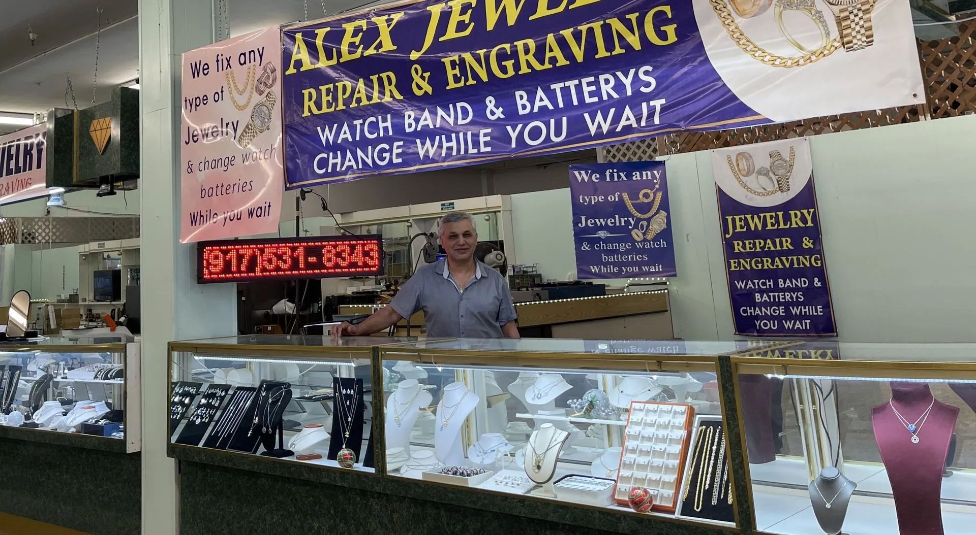 A man stands behind a counter at alex jewelers repair and engraving.