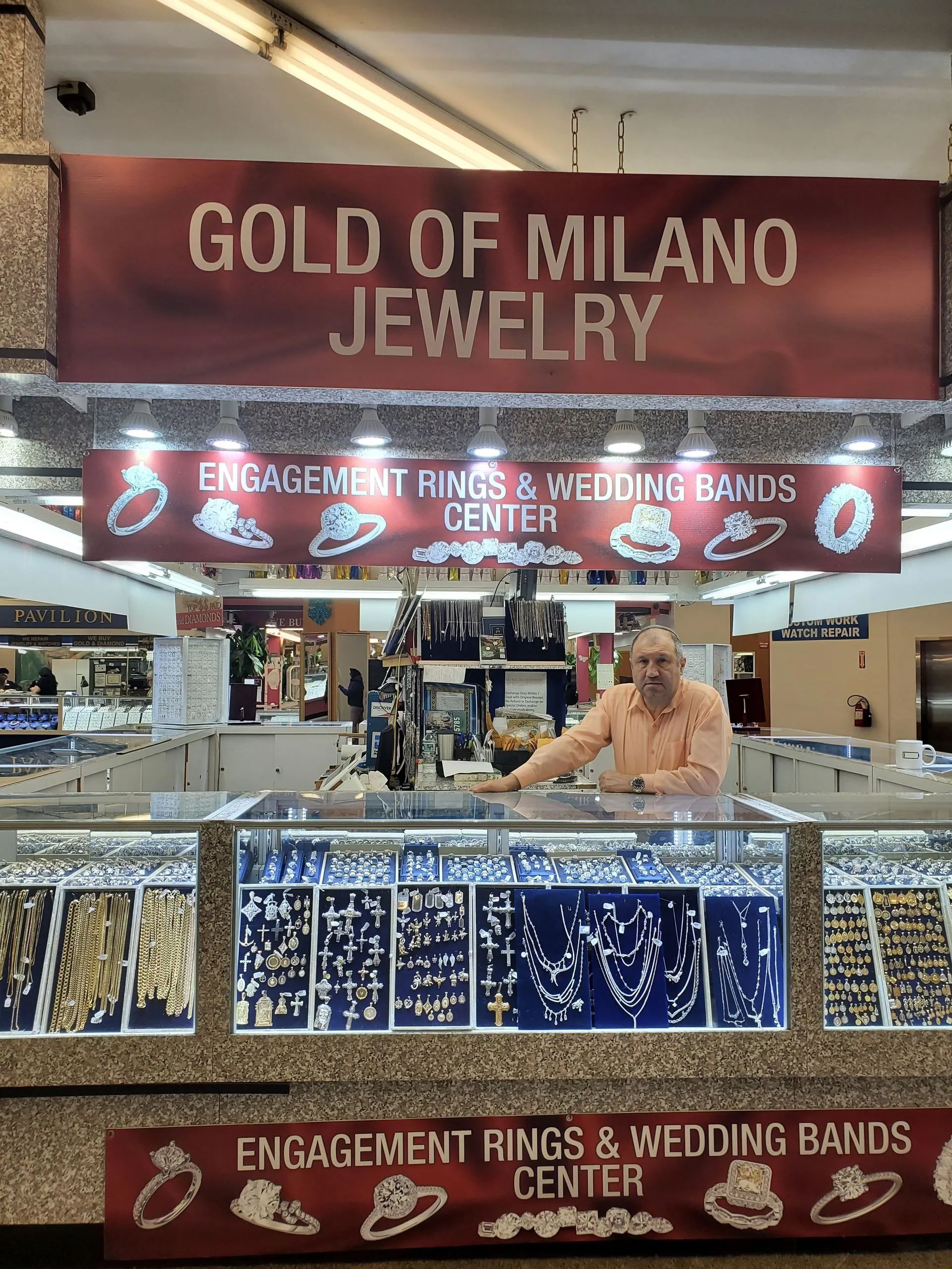 A man is standing in front of a store called gold of milano jewelry.