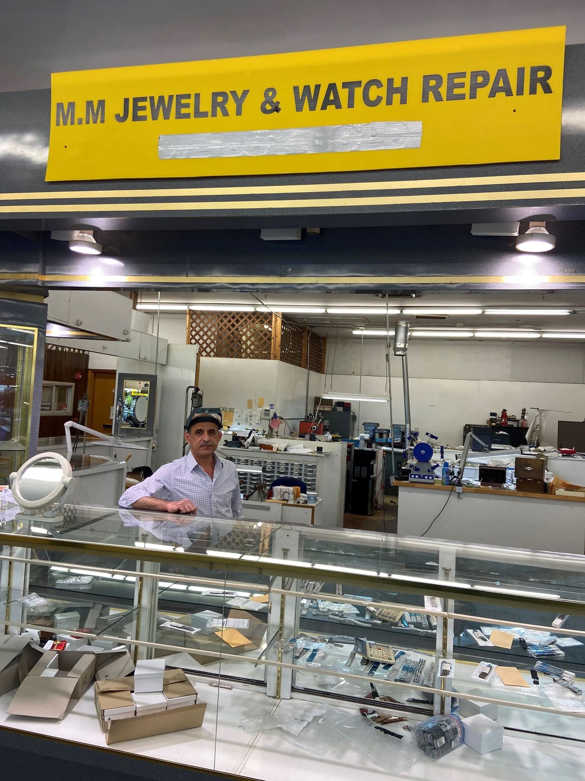 A man is standing in front of a jewelry and watch repair shop.