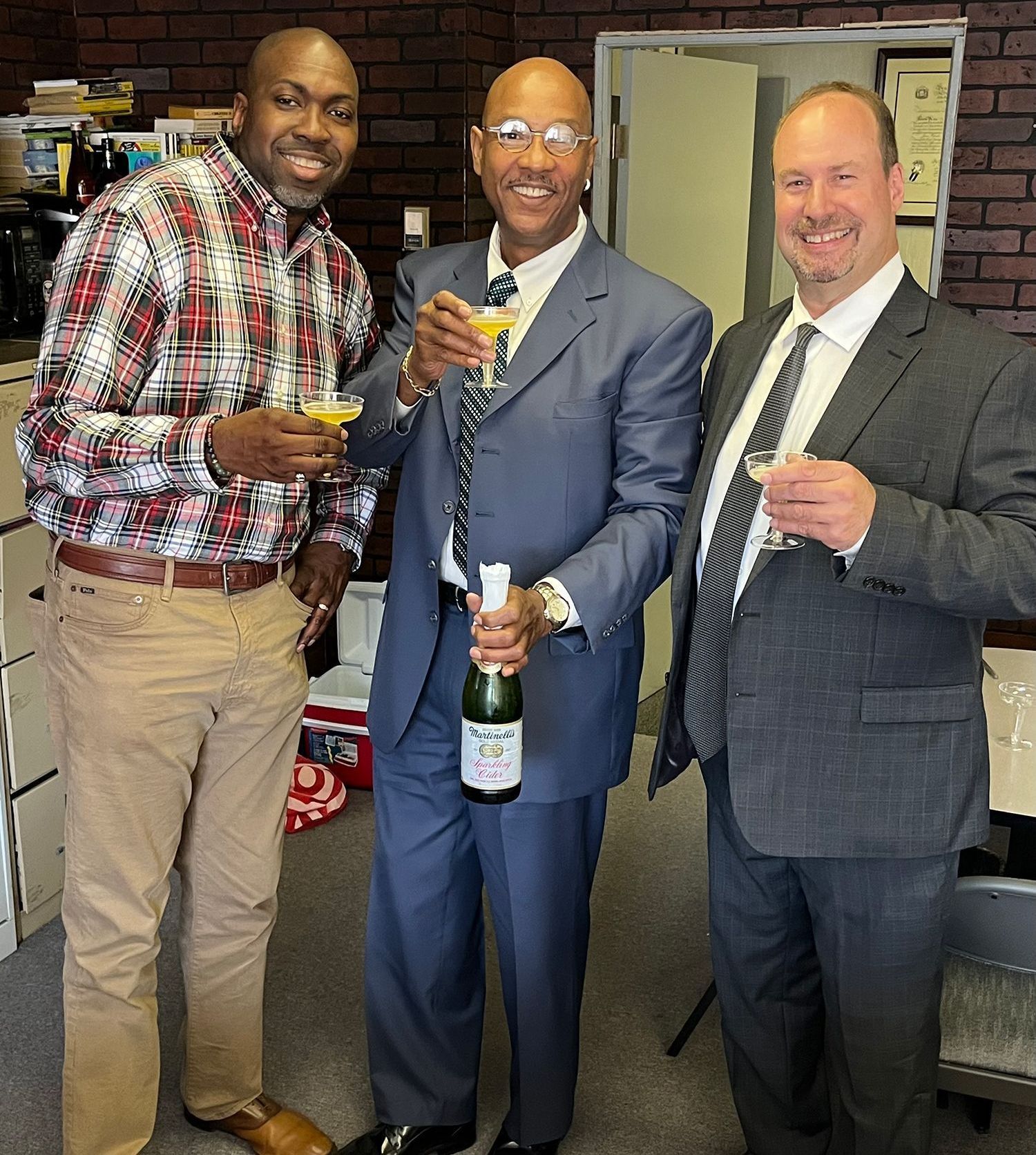 Three men standing next to each other holding wine glasses and a bottle of champagne.