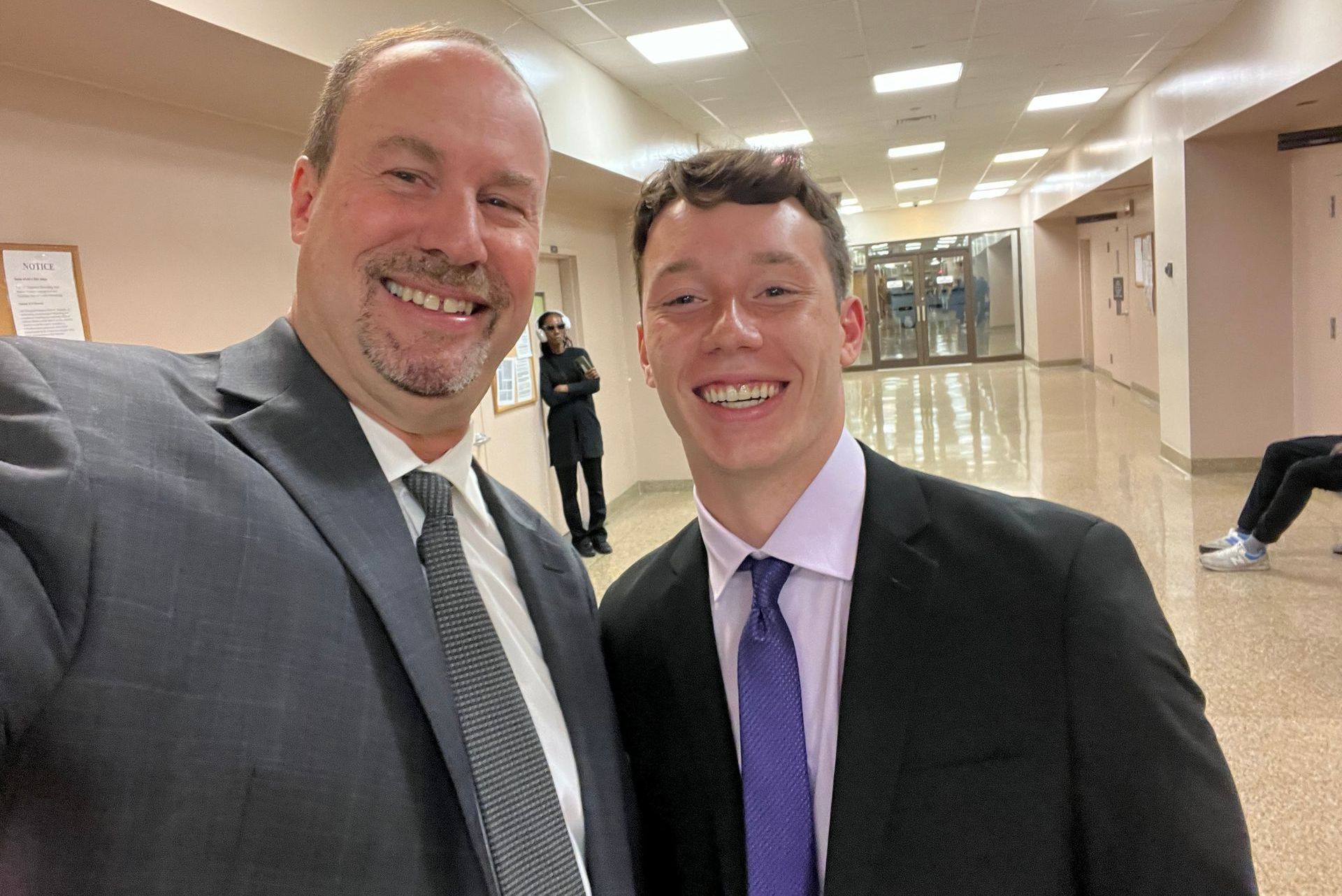 Two men in suits and ties are posing for a picture in a hallway.