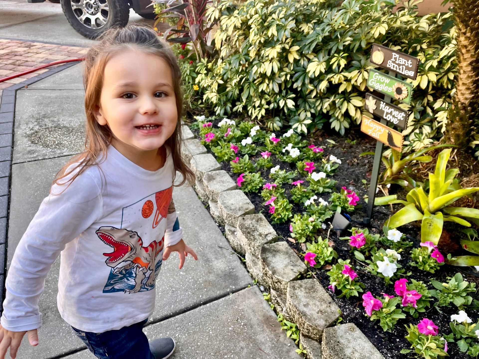 A little girl is standing in front of a flower bed.