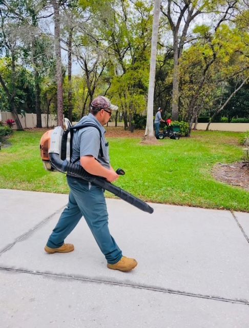 A man is walking down a sidewalk with a backpack blower on his back