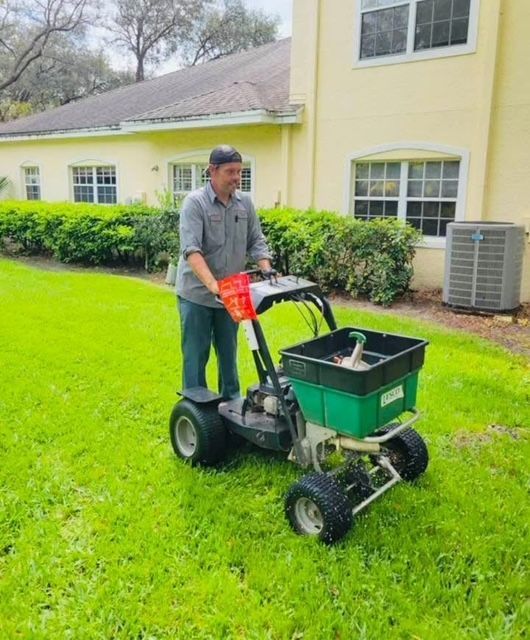 A man is spreading fertilizer on a lawn with a spreader.