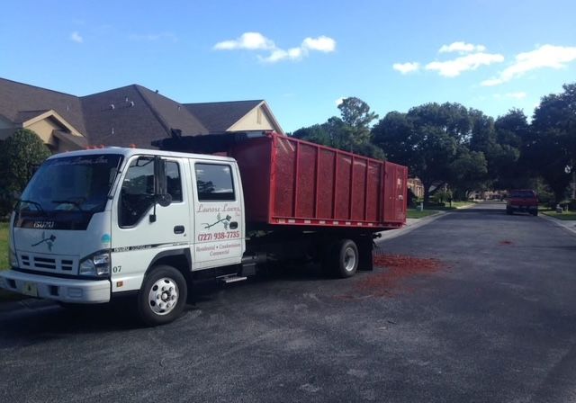 A white truck with a red dumpster is parked on the side of the road