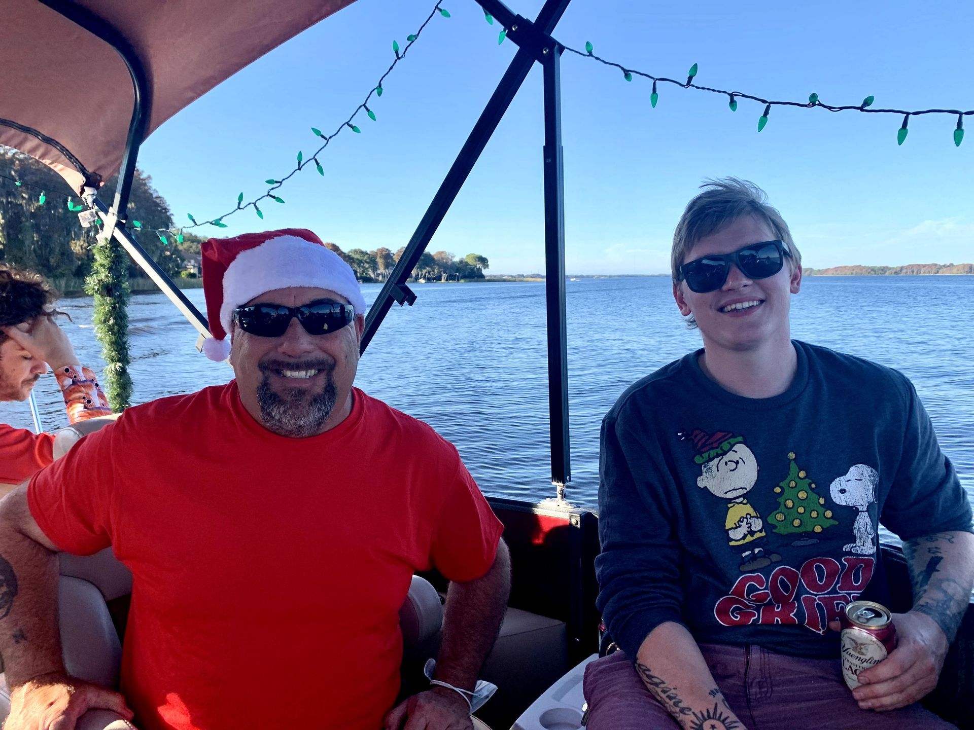 Two men are sitting on a boat wearing santa hats and sweaters.