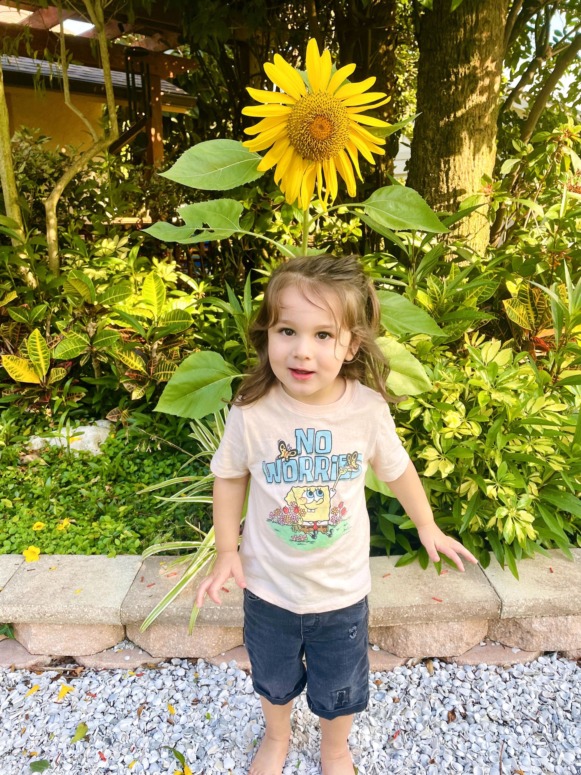A little girl is standing in front of a sunflower.