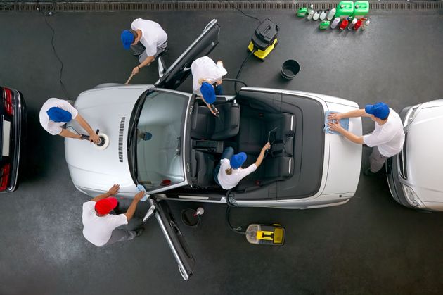 Workers cleaning a silver convertible car, using brushes and equipment in a garage.