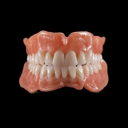 A close up of a denture with white teeth on a black background.